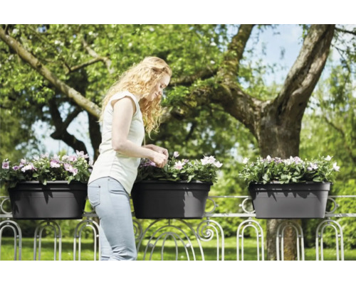 Kvinna som sköter om blommor i balkonglådor på ett balkongräcke