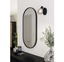 Oval spegel med lampa och dekoration på en byrå.