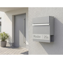 Grå brevlåda med tidningsfack på en vägg bredvid en dörr