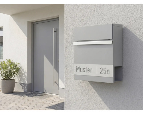 Grå brevlåda med tidningsfack på en vägg bredvid en dörr