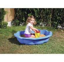 Flicka leker i en blå sandlåda med sandleksaker i trädgården.