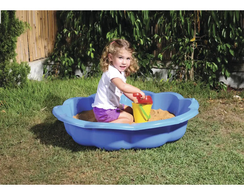 Flicka leker i en blå sandlåda med sandleksaker i trädgården.