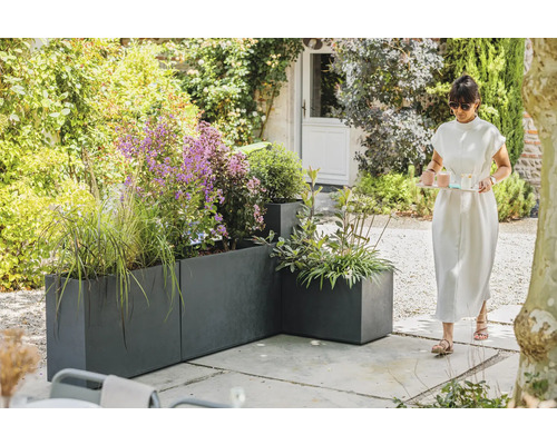 Trädgårdsvy med grå planteringskärl och en kvinna som bär en bricka