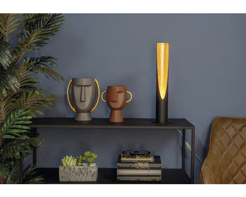 Dekorativ scen med en bordslampa, två vaser med ansikten, krukväxter och böcker på en hylla