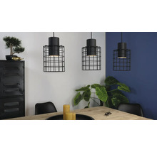 Tre pendellampor med svart trådbur ovanför ett matbord i ett ljust rum