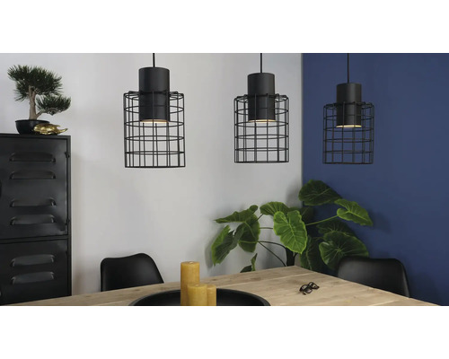 Tre pendellampor med svart trådbur ovanför ett matbord i ett ljust rum