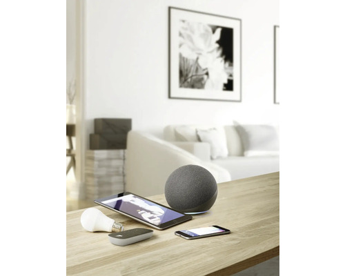 Bild av ett vardagsrum med smarta hemenheter som högtalare, surfplatta, smartphone och glödlampa på ett bord.