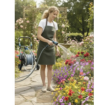 En kvinna vattnar blommor med en trädgårdsslang i en frodig trädgård med rosenbåge