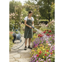 Kvinna vattnar blommor med en trädgårdsslang bredvid en slangvagn i en blomsterträdgård.