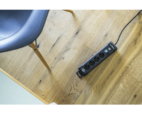 Grenuttag med överspänningsskydd och strömbrytare på trägolv.