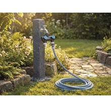 Trädgårdsscen med vattenkran, fördelare och trädgårdsslang på en gräsmatta