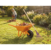 Trädgårdsscen med skottkärra, kratta och barn som samlar löv