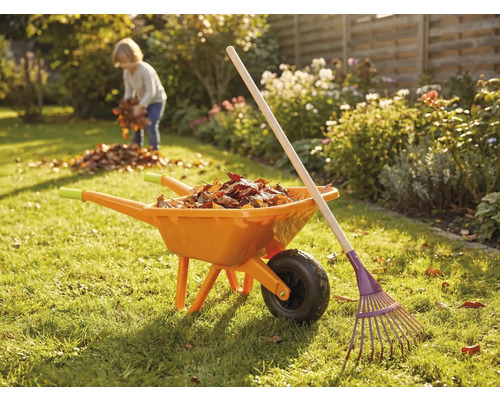 Trädgårdsscen med skottkärra, kratta och barn som samlar löv