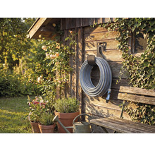 Trädgårdsscen med slangvinda på trävägg, omgiven av växter