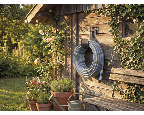 Trädgårdsscen med slangvinda på trävägg, omgiven av växter