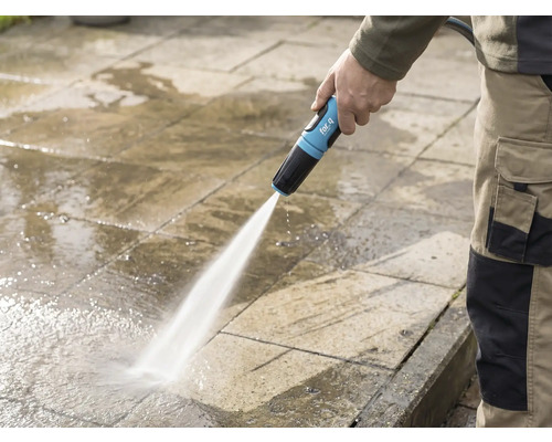 En person rengör en stenterass med en for_q trädgårdsslang