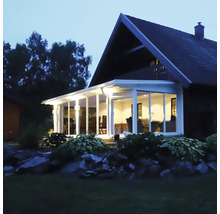Upplyst uterum med vit aluminiumstomme och glaselement vid ett hus i skymningen.
