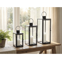 Tre dekorativa lyktor av metall och glas med ljus på ett bord.