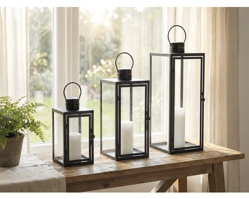 Tre dekorativa lyktor av metall och glas med ljus på ett bord.