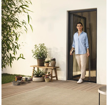 Kvinna går in på terrassen genom en insektsdörr, omgiven av växter och trädgårdstillbehör.