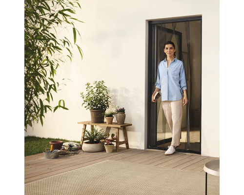 Kvinna går in på terrassen genom en insektsdörr, omgiven av växter och trädgårdstillbehör.