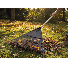 Lövraka med träskaft i bruk på en gräsmatta med höstlöv