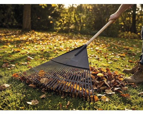 Lövraka med träskaft i bruk på en gräsmatta med höstlöv