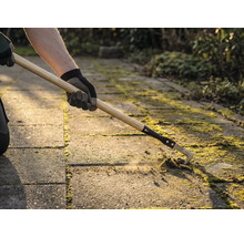 En person tar bort mossa mellan stenplattor med en fogkrats.