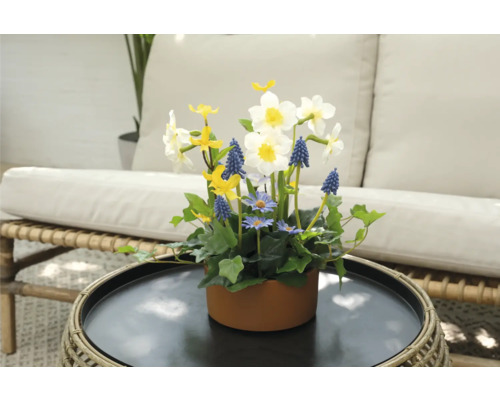 Blomsterarrangemang med påskliljor, pärlhyacinter och prästkragar i en brun kruka på ett bord