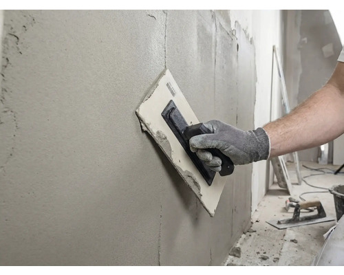 Hantverkare jämnar ut väggen med en spackelspade och filler.