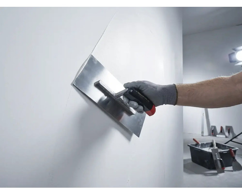 Hand med putsglättare som jämnar ut en vägg
