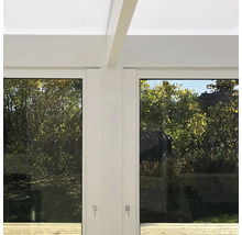 Modern vit terrassövertäckning med ljusgenomsläppligt tak, glasskjutväggar och utsikt mot trädgården.