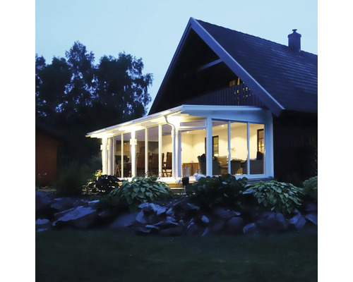 Upplyst uterum med vit aluminiumstomme och glaselement vid ett hus i skymningen.