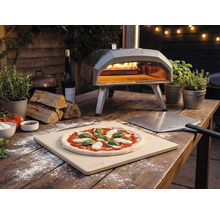Utomhusbild av en Ooni pizzaugn med pizza, pizzaspade och ingredienser på ett träbord.