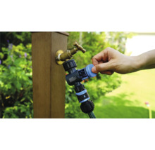 Trädgårdskran med vattenfördelare och ansluten trädgårdsslang i användning.