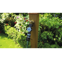 Trädgårdsscen med vattenkran på trästolpe och ansluten trädgårdsslang