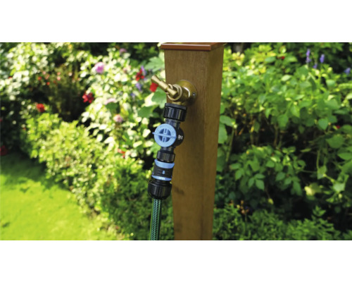 Trädgårdsscen med vattenkran på trästolpe och ansluten trädgårdsslang