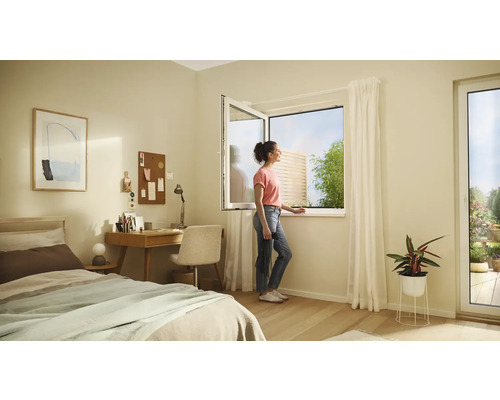 Ljust sovrum med säng, skrivbord och en kvinna som öppnar ett fönster med utsikt över trädgården.