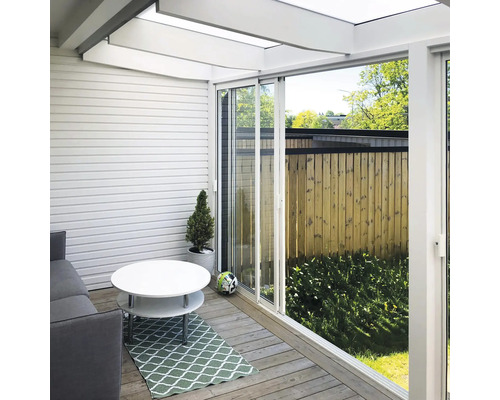 Modern terrasinglasning med vita skjutdörrar, trädäck, soffa och ljust glastak.