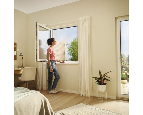 Ljust sovrum med ett fönster som kan öppnas och en kvinna som tittar ut