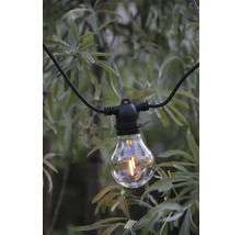 LED-filamentlampa på en svart kabel till en ljusslinga framför en grön buske.