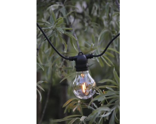 LED-filamentlampa på en svart kabel till en ljusslinga framför en grön buske.