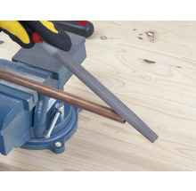 Ett kopparrör bearbetas med en fil som är fäst i ett skruvstäd.