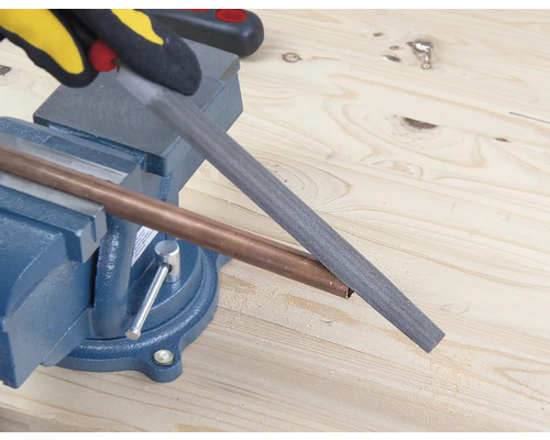 Ett kopparrör bearbetas med en fil som är fäst i ett skruvstäd.