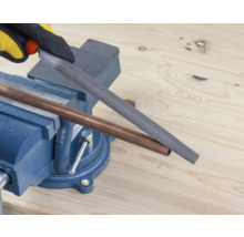 Ett kopparrör bearbetas med en fil som är fastklämd i ett skruvstycke.