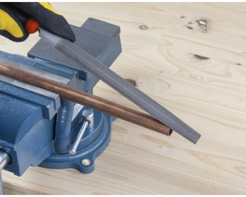 Ett kopparrör bearbetas med en fil som är fastklämd i ett skruvstycke.