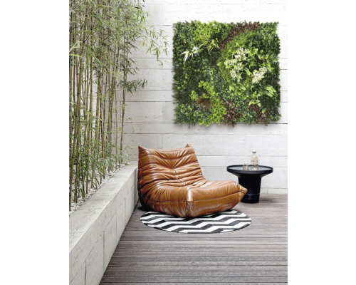 Miljö med en fåtölj, ett bord, en rund matta och en grön väggpanel på en terrass