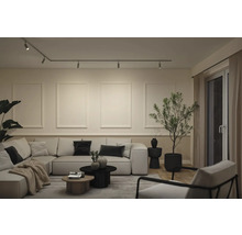 Modernt vardagsrum med ljus hörnsoffa, skensystem med spotlights i taket och dekorativ väggpanel med ramlister.