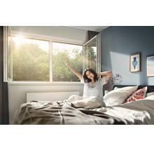 Ljust sovrum med ett vidöppet plastfönster där solljuset strömmar in och en person i sängen som sträcker på sig vid uppvaknande.