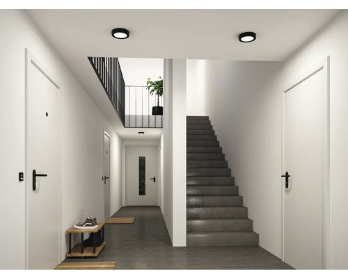 Modern, ljus hall med vita dörrar, svarta handtag, en mörk betongtrappa och runda svarta taklampor.